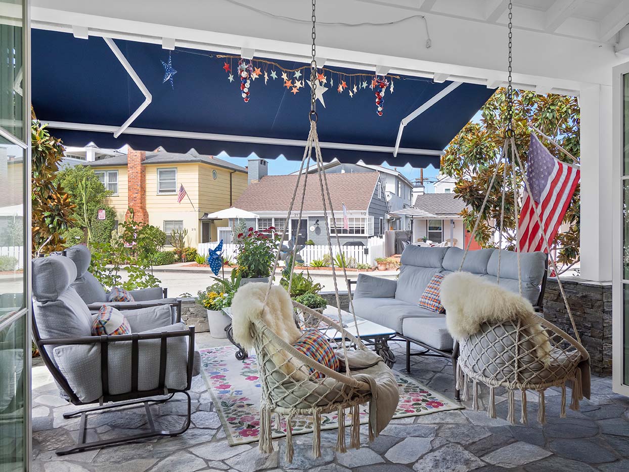 Covered patio at 220 Collins with hanging macrame swing chairs, sofa seating, and an American flag