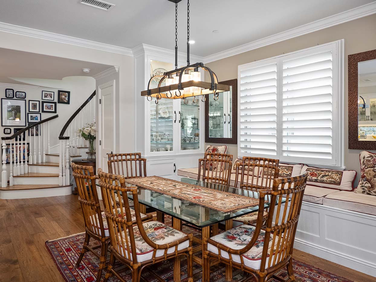 Dining room at 220 Collins with a glass-top rattan table and chairs, a built-in china cabinet, and plantation shutters