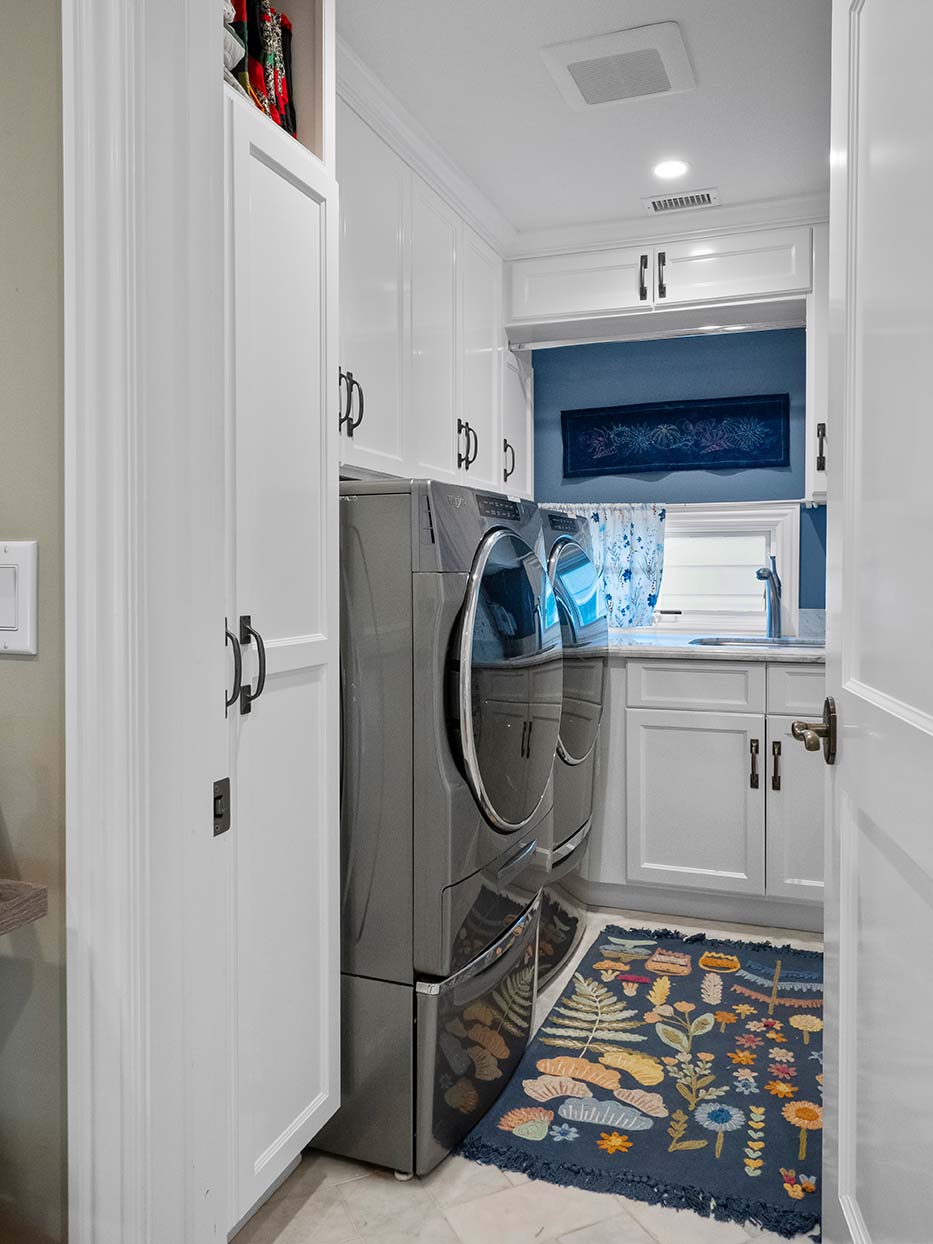 Laundry room at 220 Collins with a stacked washer and dryer, a navy accent wall, and a floral rug