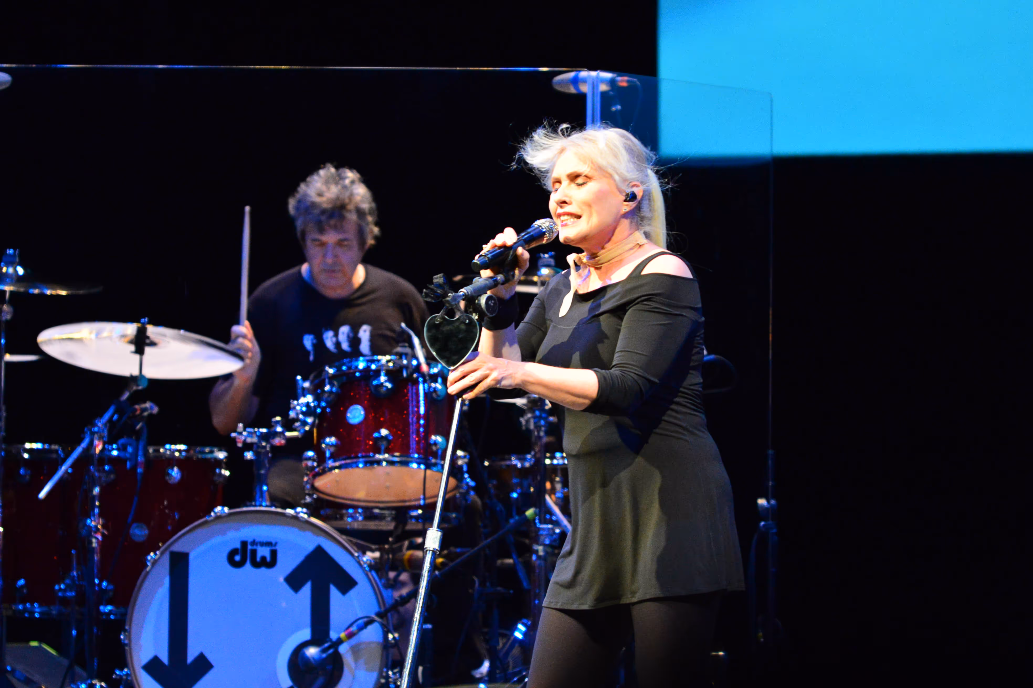 Blondie mid performance. She is pulling the microphone stand toward her, with an expression of concentration on her face. 