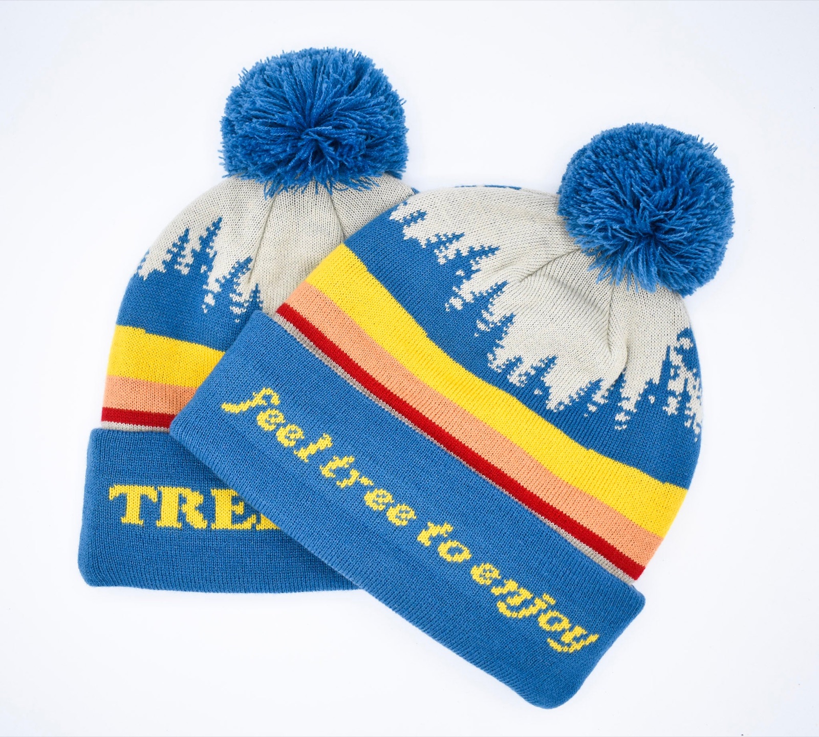 Two Retro Treehaus pom beanies in blue and cream with the sunset stripes and feel tree to enjoy stitched on the cuff