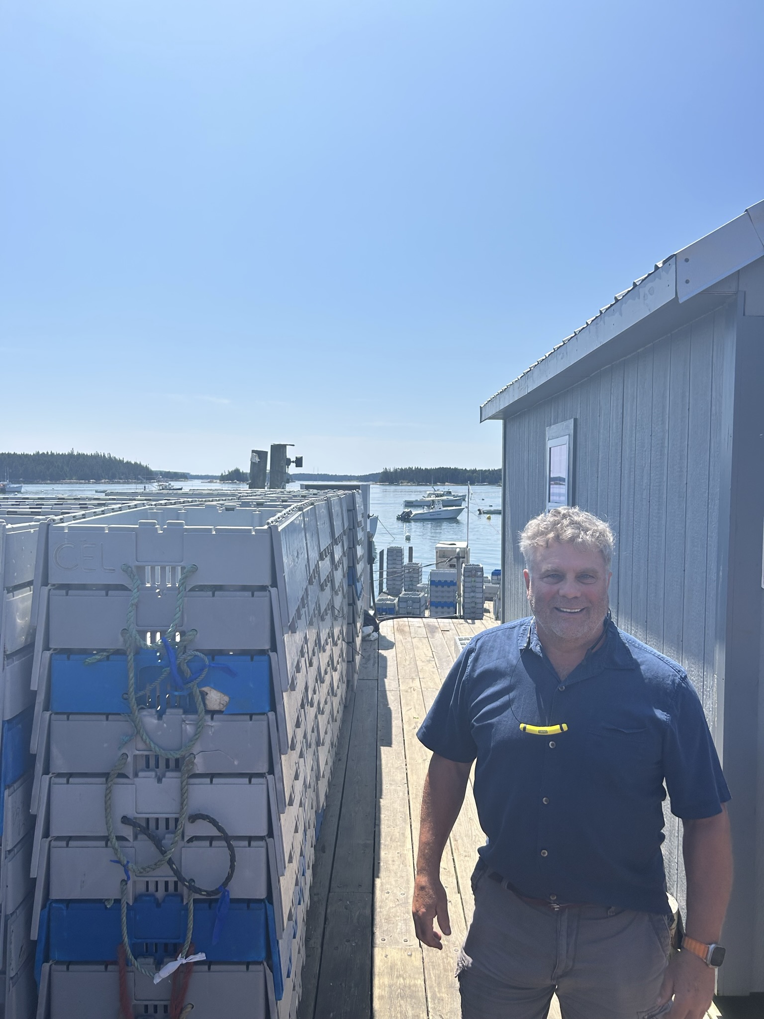 Bruce Hannough beside a wall of stacked Trident reusable plastic containers on a Maine working dock