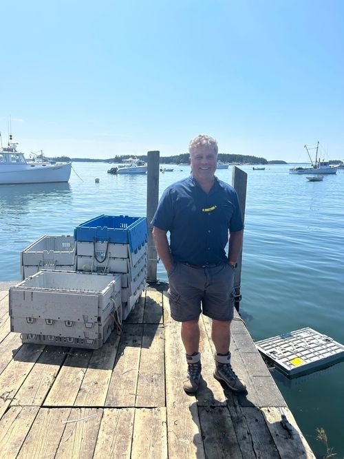 Bruce Hannough on the dock at Kittery Point Maine with Trident reusable plastic containers and lobster fleet in background