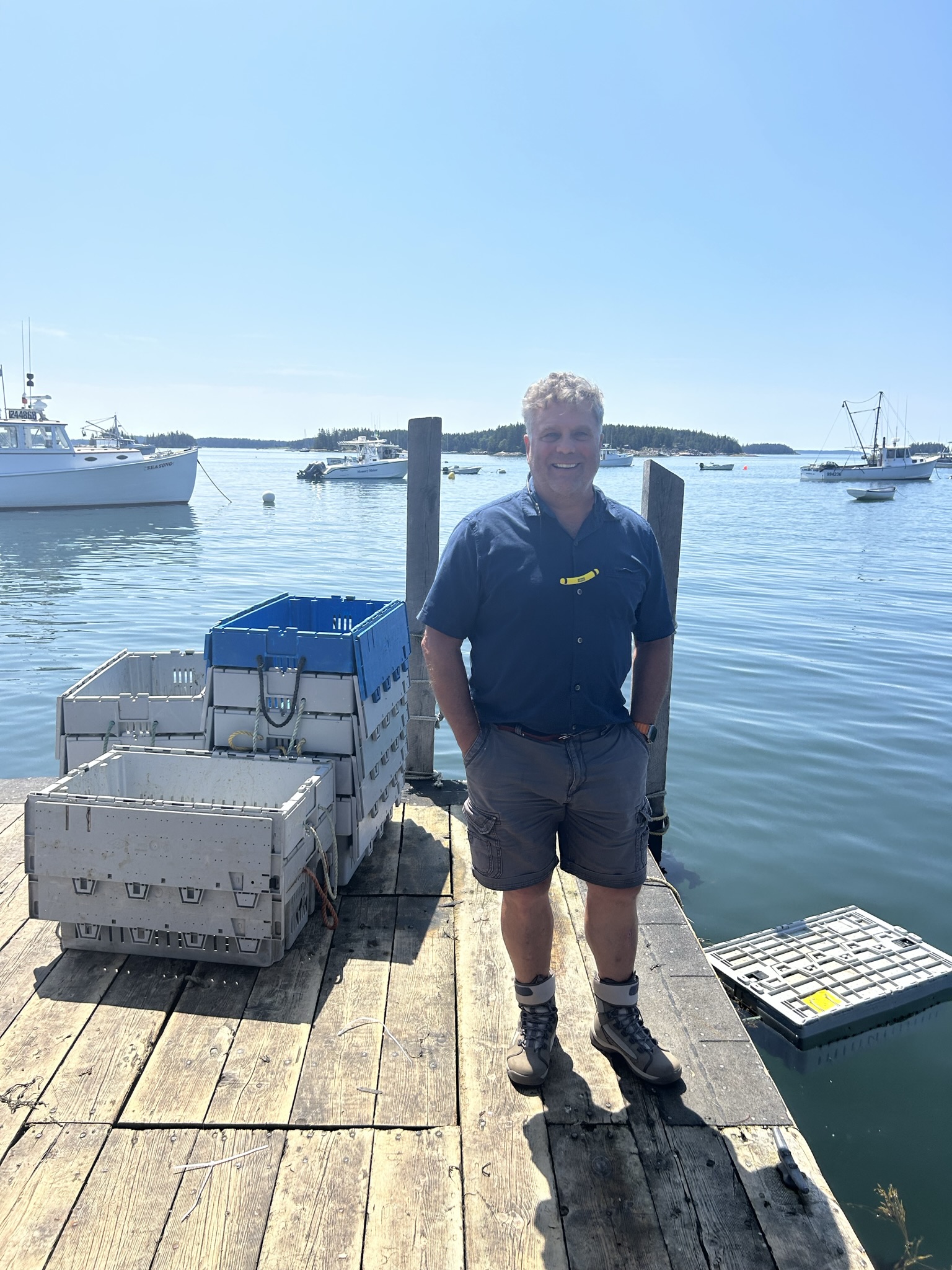Bruce Hannough on the dock at Kittery Point Maine with Trident reusable plastic containers and lobster fleet in background