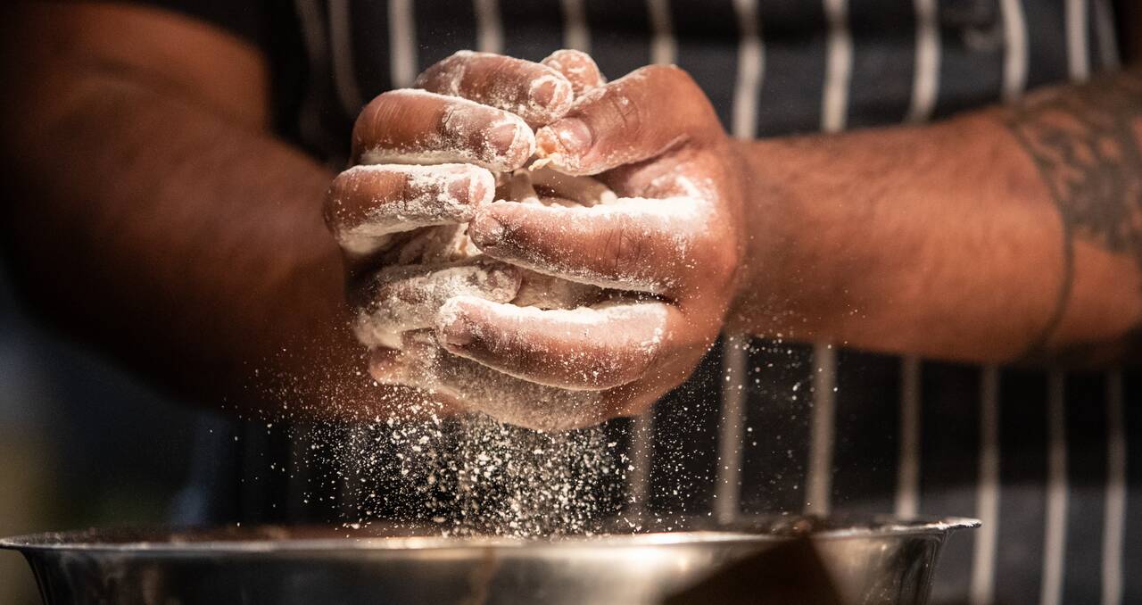 Mãos de uma pessoa mexendo em uma massa e preparando uma comida, possivelmente fazendo comidas para vender.