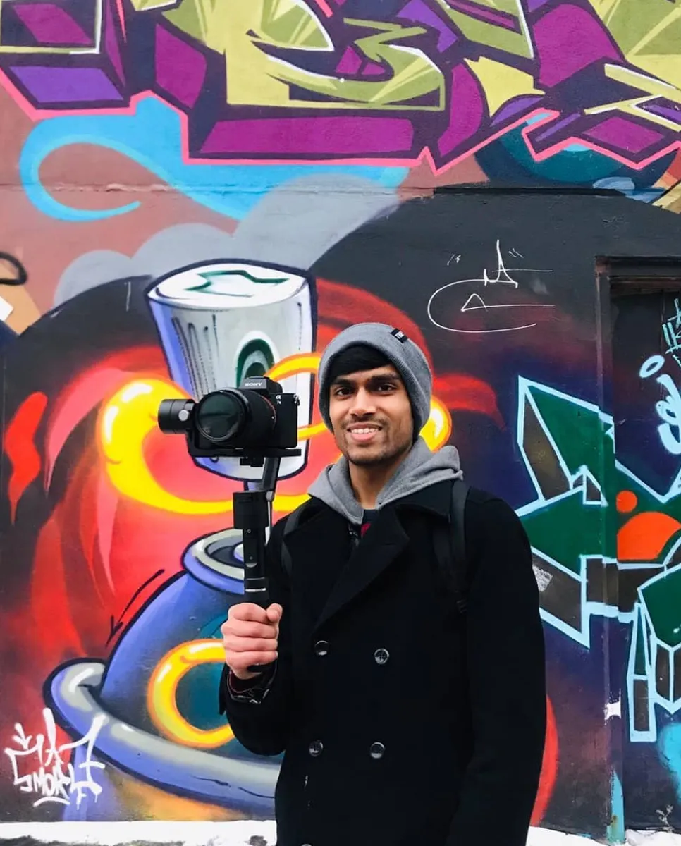 Vinit holding a camera stabilizer while standing in front of graffiti art