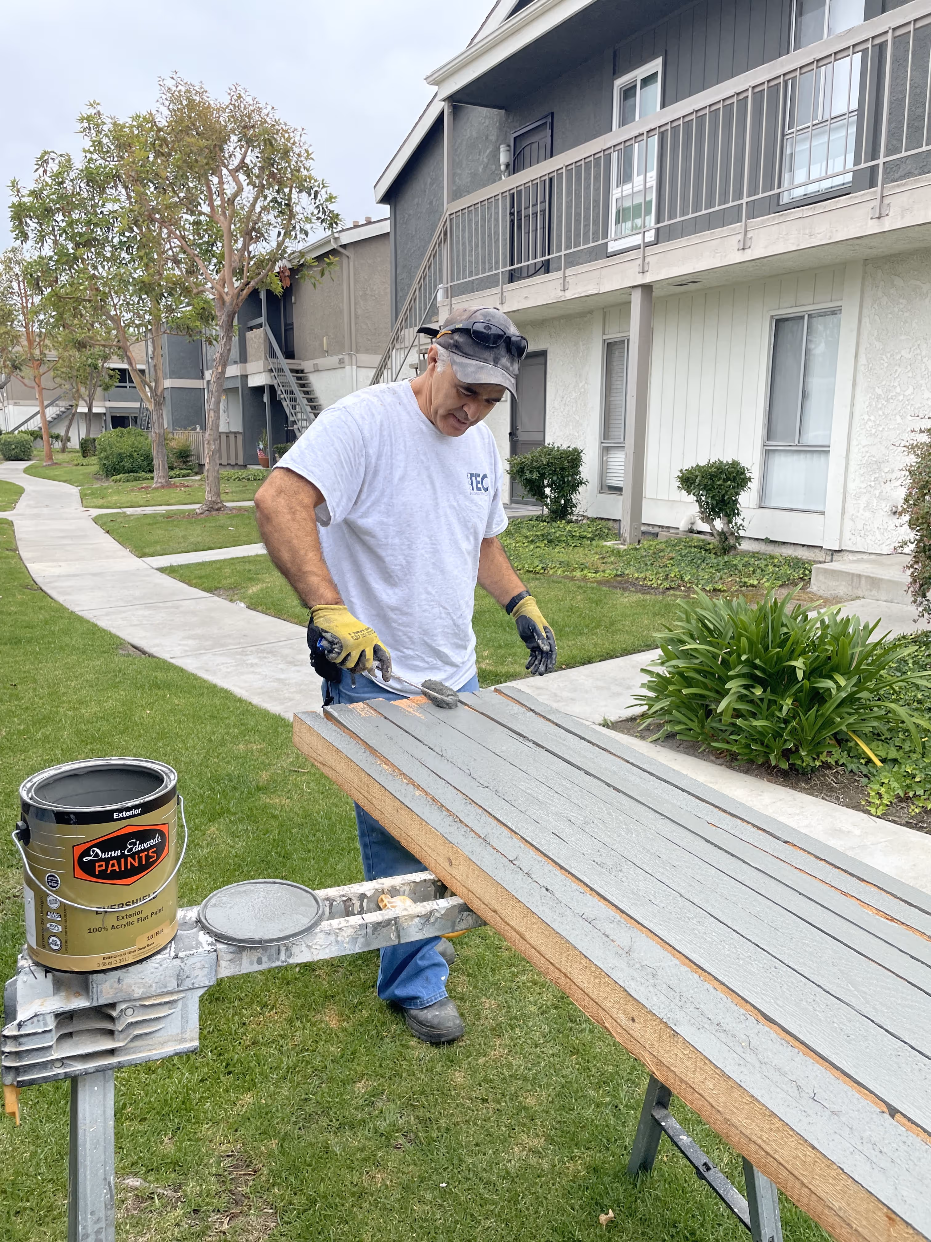 A man in a white shirt is painting a wooden bench.