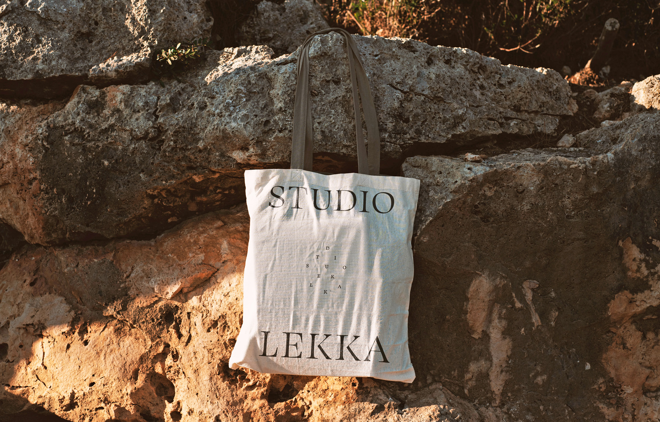 A Studio Lekka tote bag against a Mediterranean stone wall.
