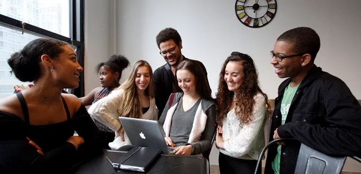 A bunch of people all viewing something important on a laptop screen. 