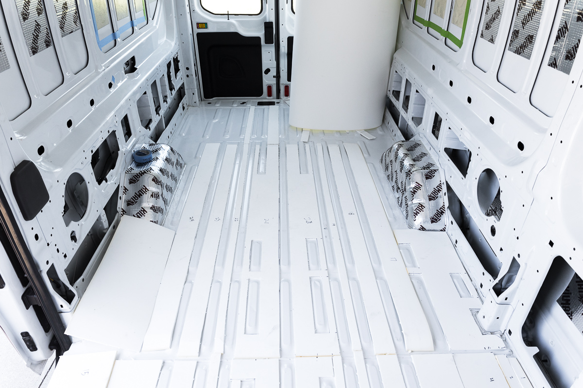 Looking down at the floor of an empty cargo van with the metal corrugations filled with white minicell foam insulation