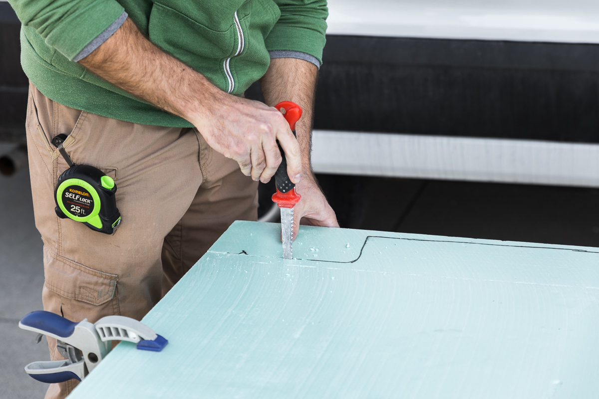 Close up on a man cutting a piece of green XPS foam board using a drywall saw