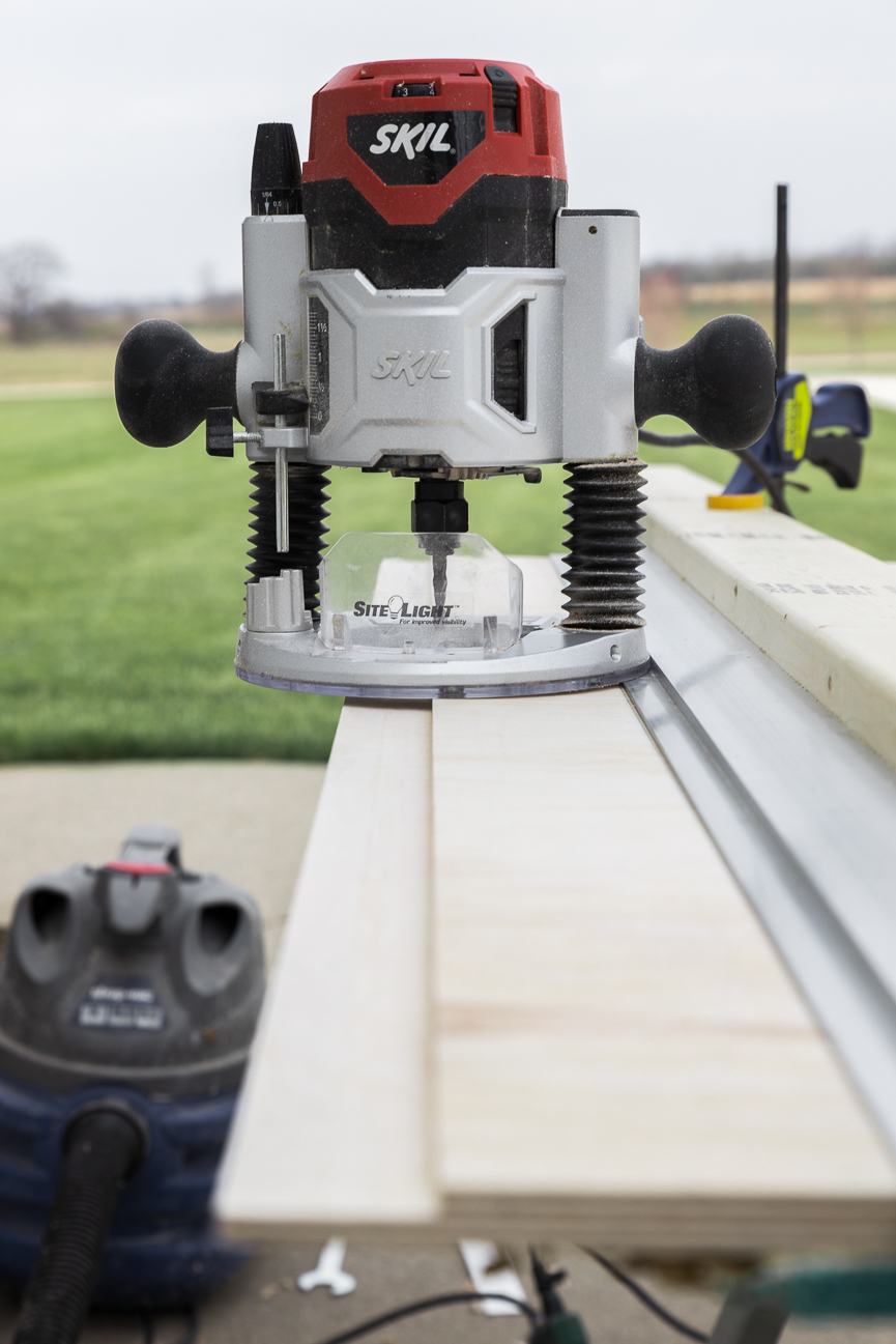 Looking down a piece of plywood as a 'rabbit' cut for edge joinery with a straight edge clamped to the wood and a router resting on top of it