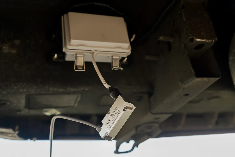 A box mounted underneath a vehicle with a small electrical adapter hanging from it with wires coming from either end