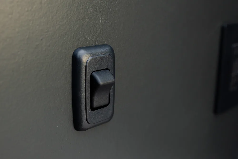 Close up on a minimalist black switch installed on the face of a black cabinet