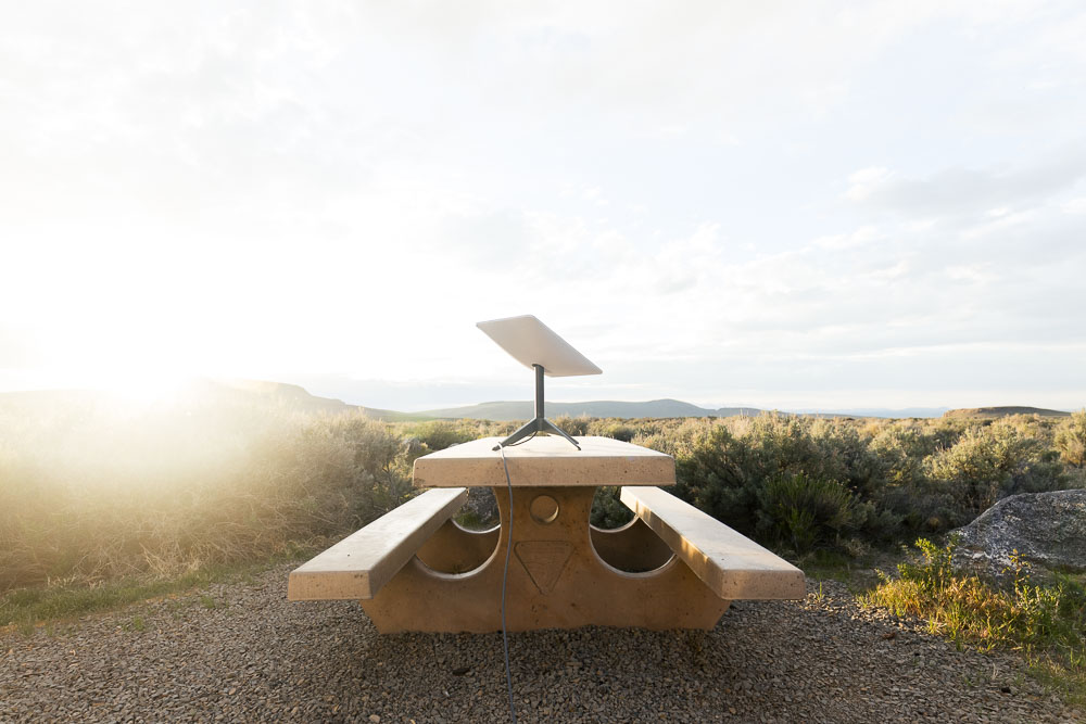 A Starlink dish set up on a picnic table with mountain views in the distance