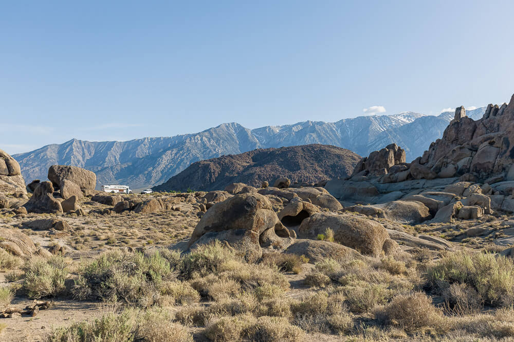 Two vehicles are parked in a secluded campsite among the boulders of the Alabama Hills with mountain peaks in the background