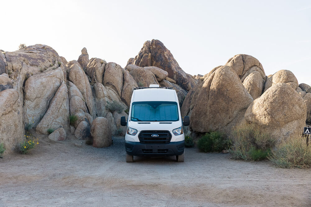 A campervan parked in a small primitive campsite surrounded by large boulders