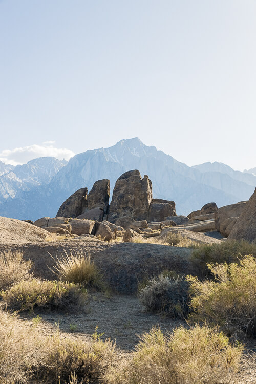 A rock formation surrounded by scrubby bushes and framed by a larger silhouetted of a mountain peak in the distance