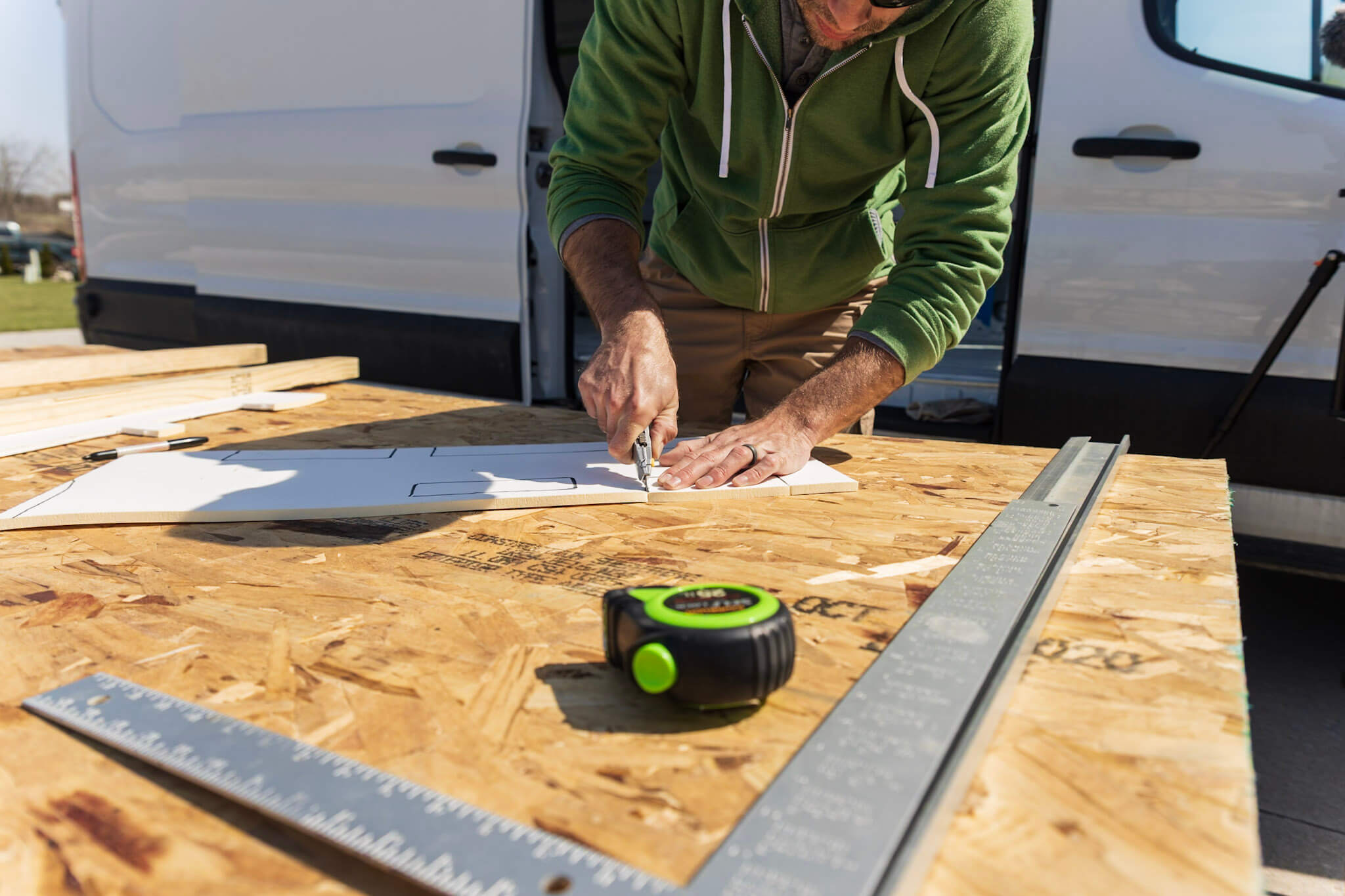 A man working with tools on a makeshift table with a campervan in the background behind him