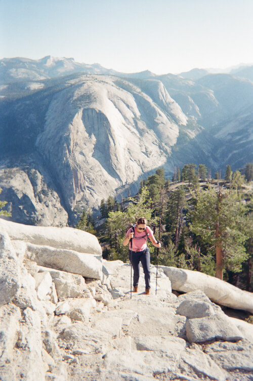 A woman hiking on open granite rock with large mountain views in the distance 