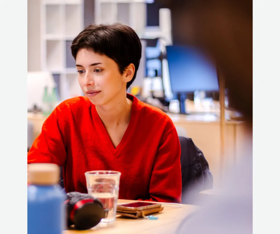 Vrouw in een rode top aan een bureau met beeldschermen