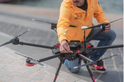 A person in a yellow jacket holding a droneAI-generated content may be incorrect.