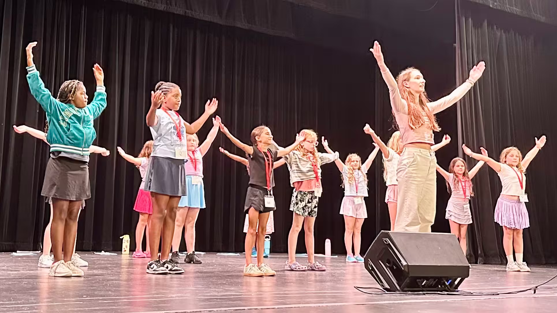 Children and a young instructor on stage with arms raised