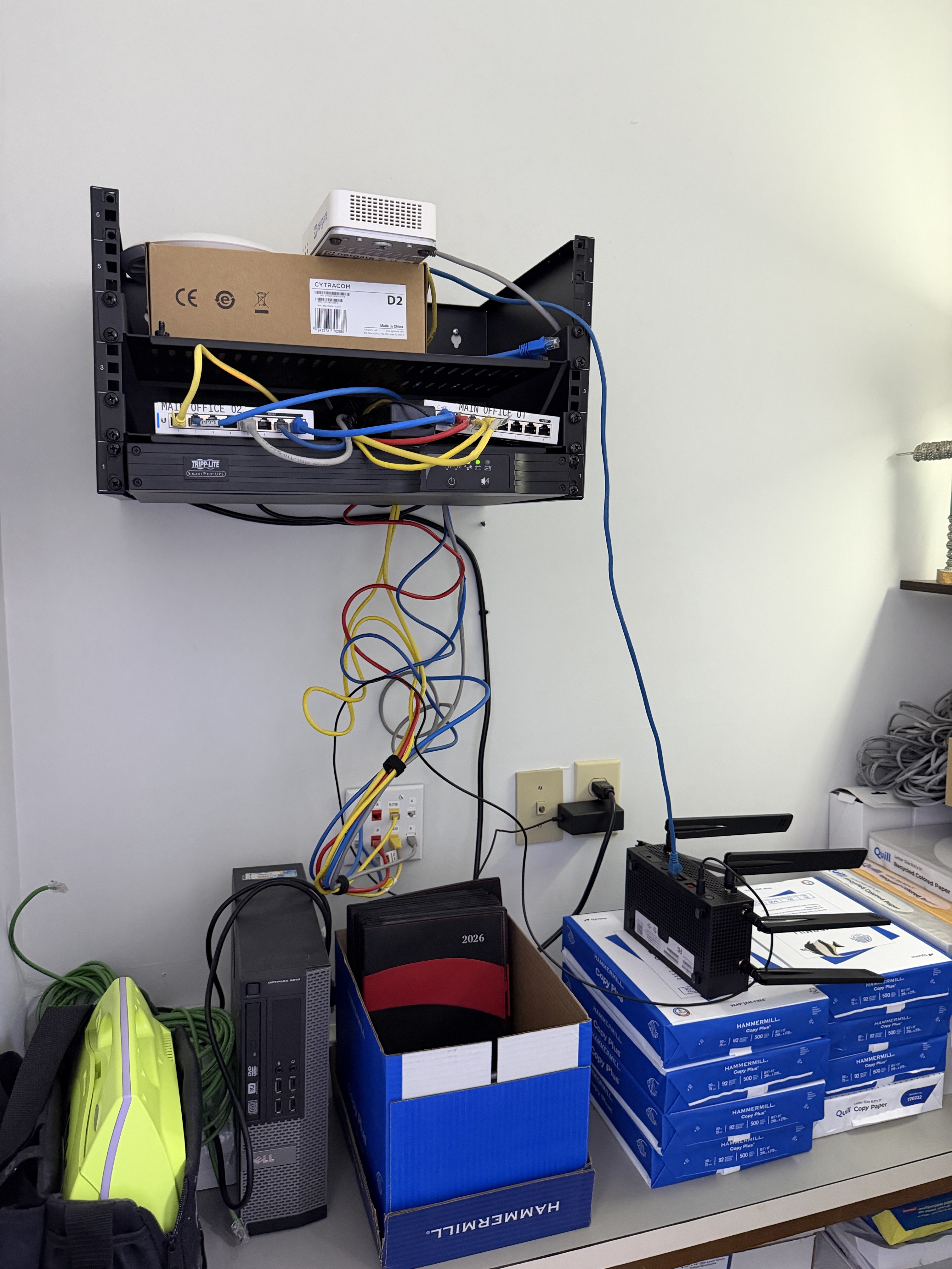 Original wall-mounted small business network rack with messy Ethernet cables and unorganized network equipment before the upgrade.