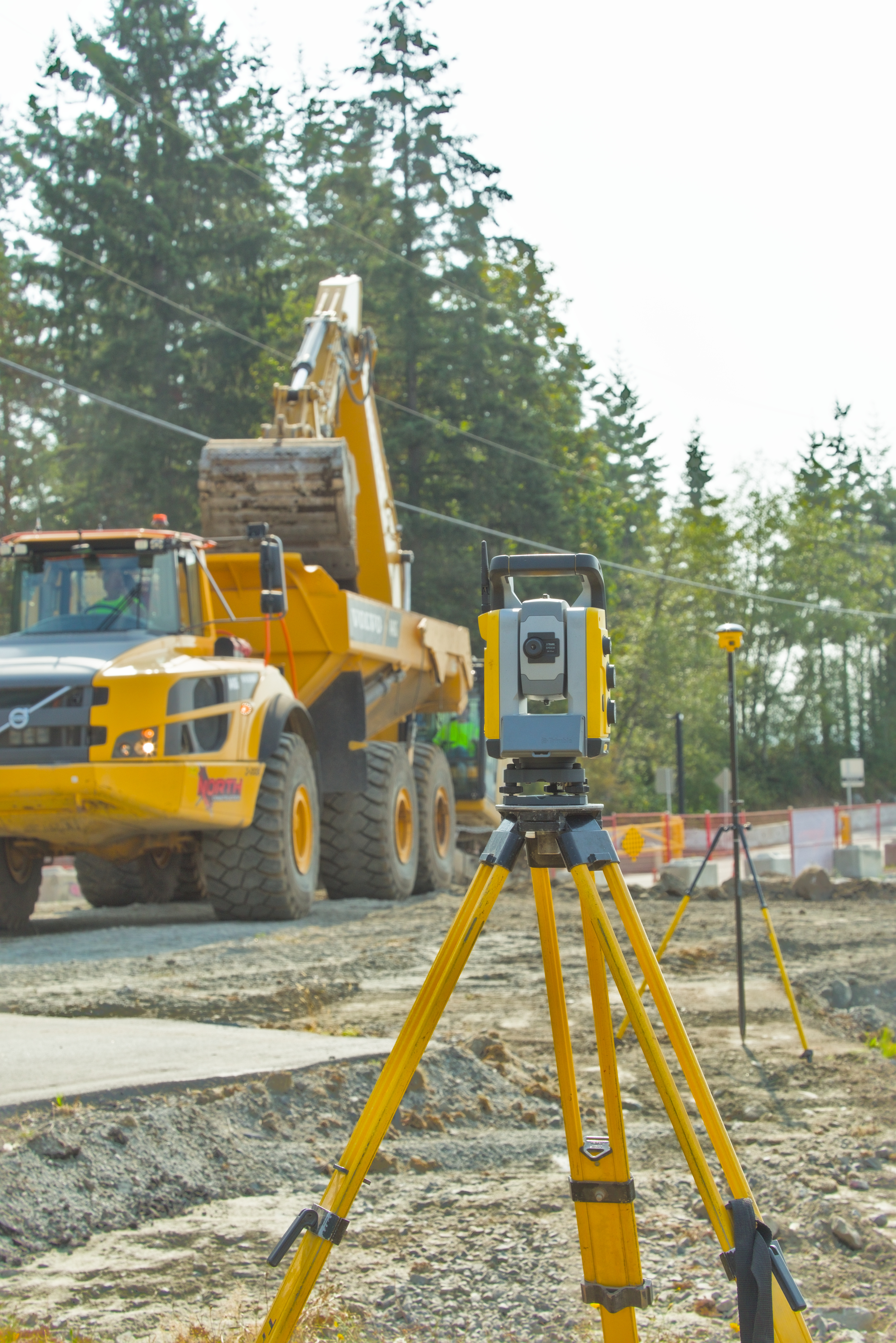 Robotic total station on tripod with haul truck and excavator on a construction site