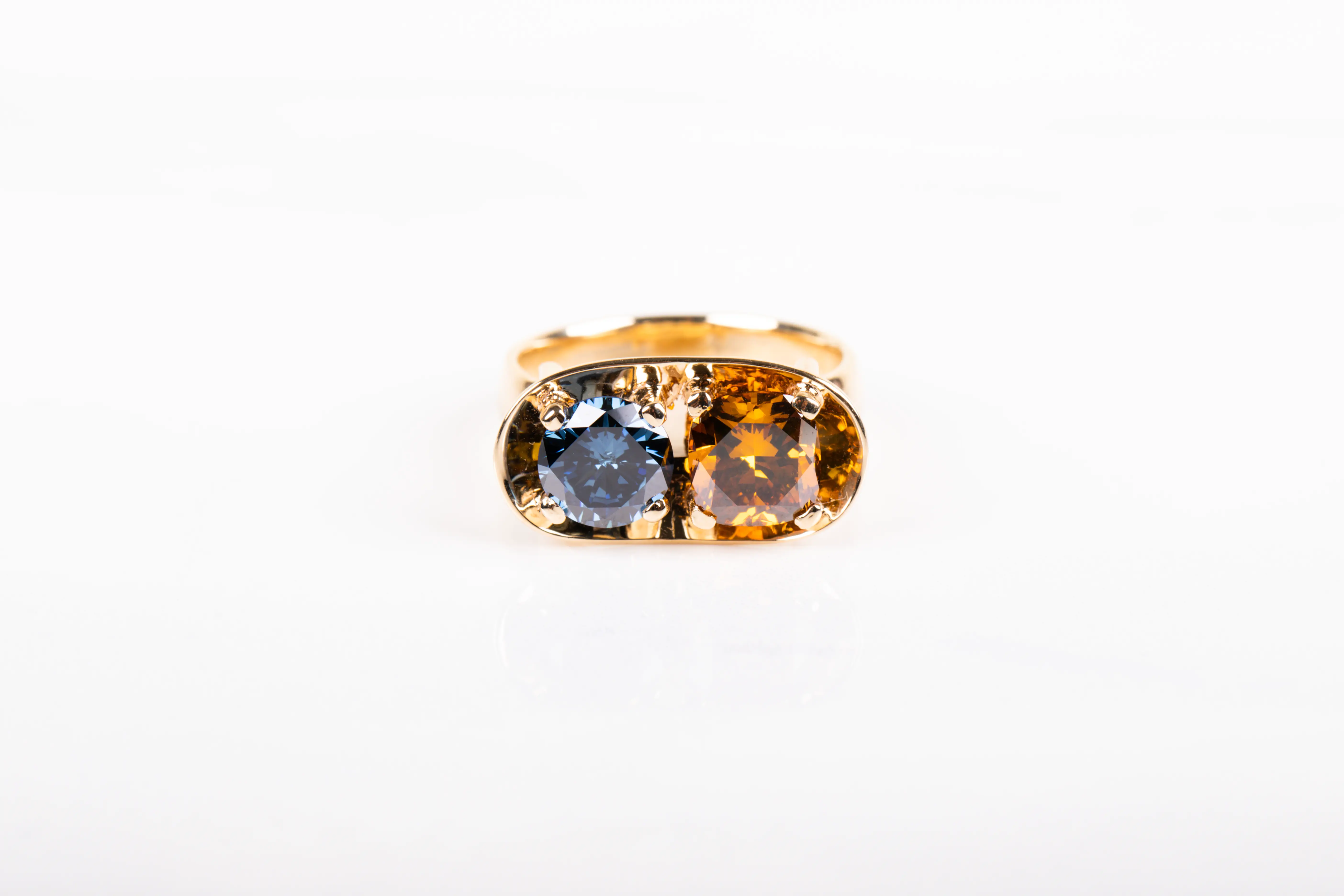 The photo of a gold jewelry setting with a blue and a yellow diamond