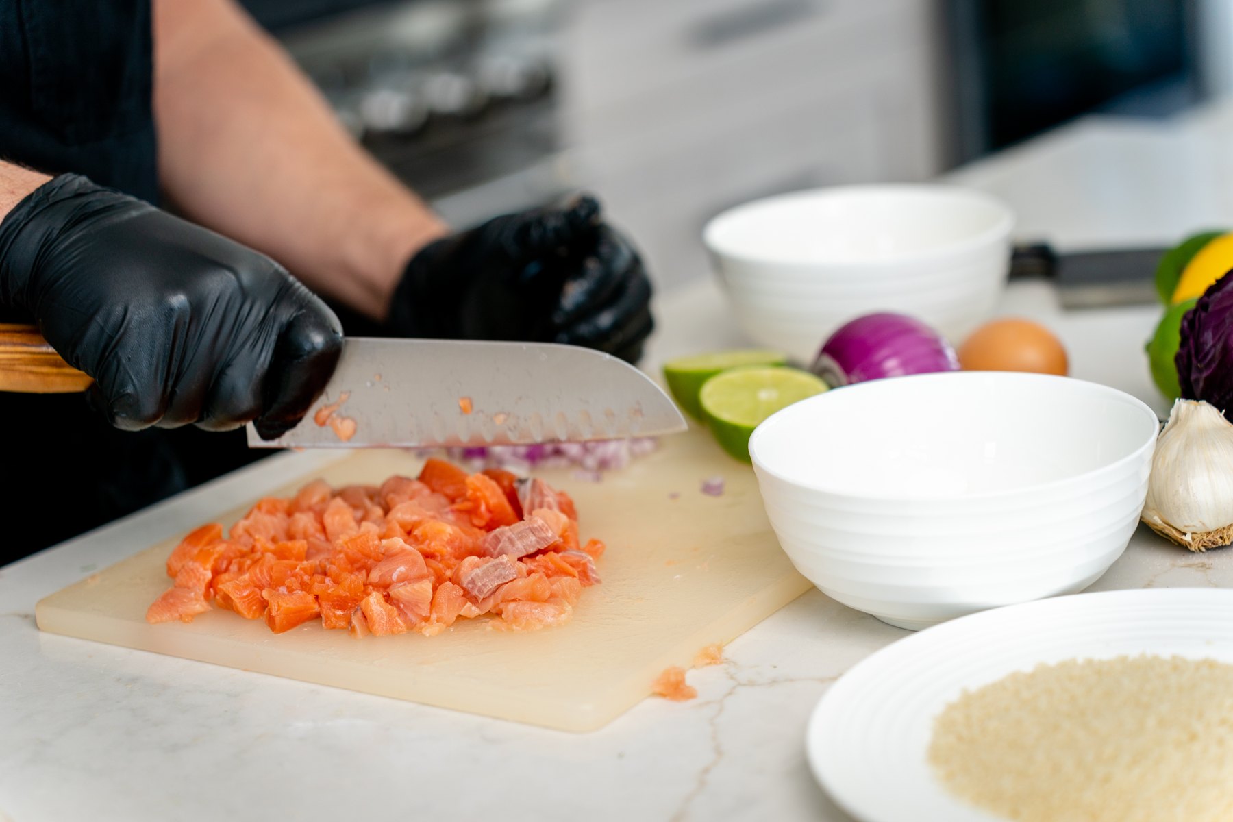 Hand chopping salmon into a rough dice on a cutting board