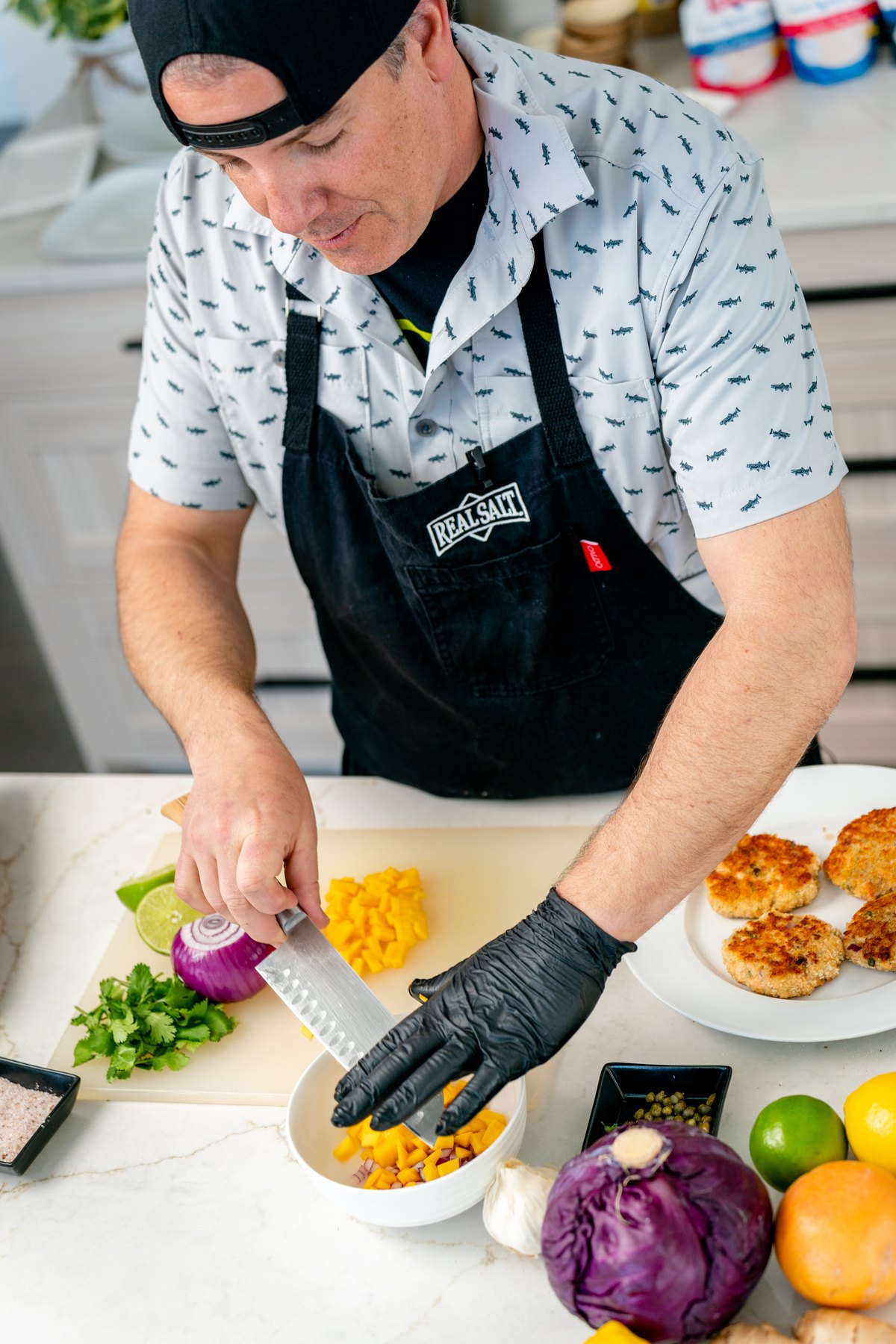 Dicing mango on a cutting board next to chopped red onion and cilantro