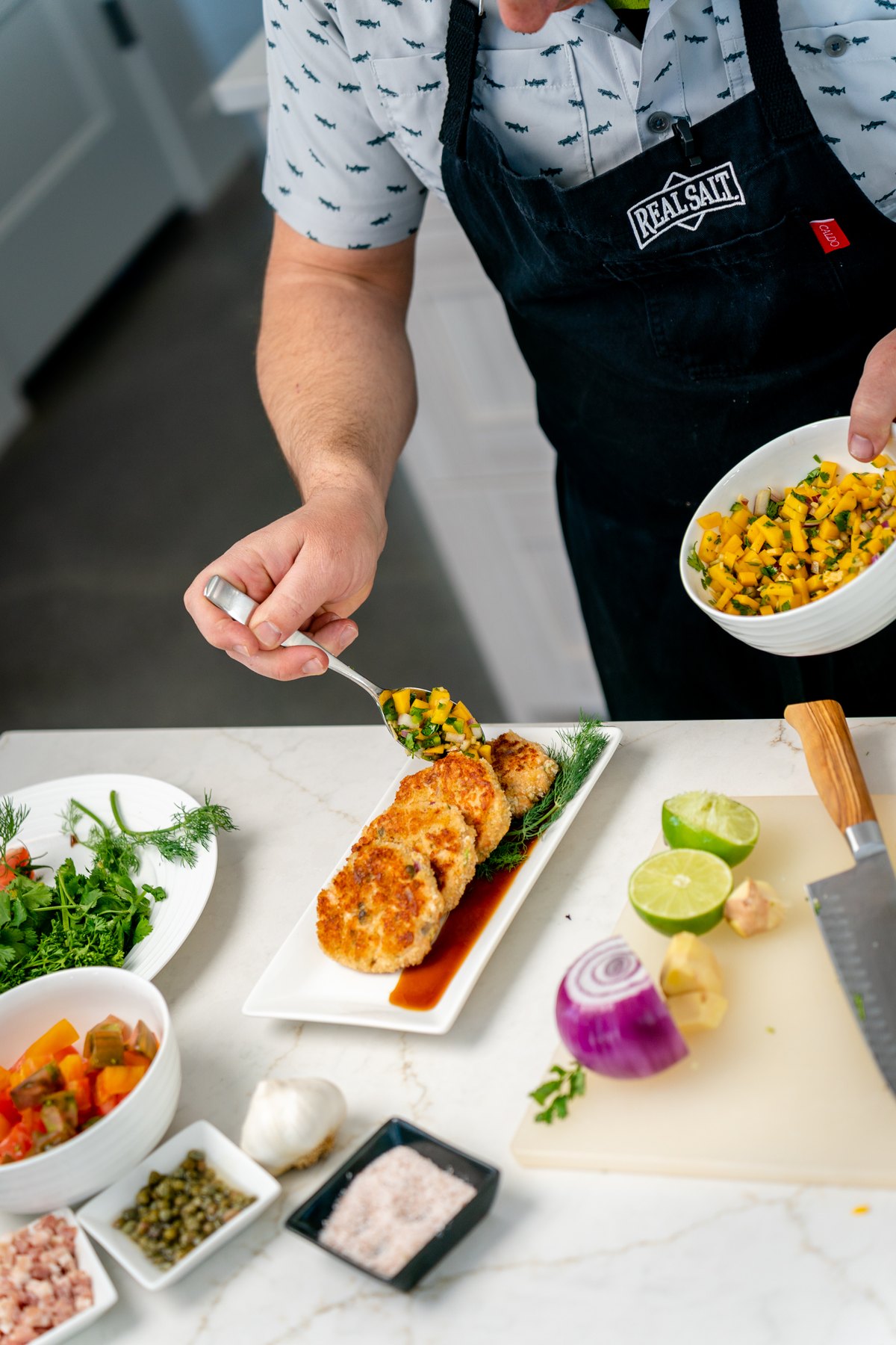 Spooning mango salsa over salmon cakes on a white platter