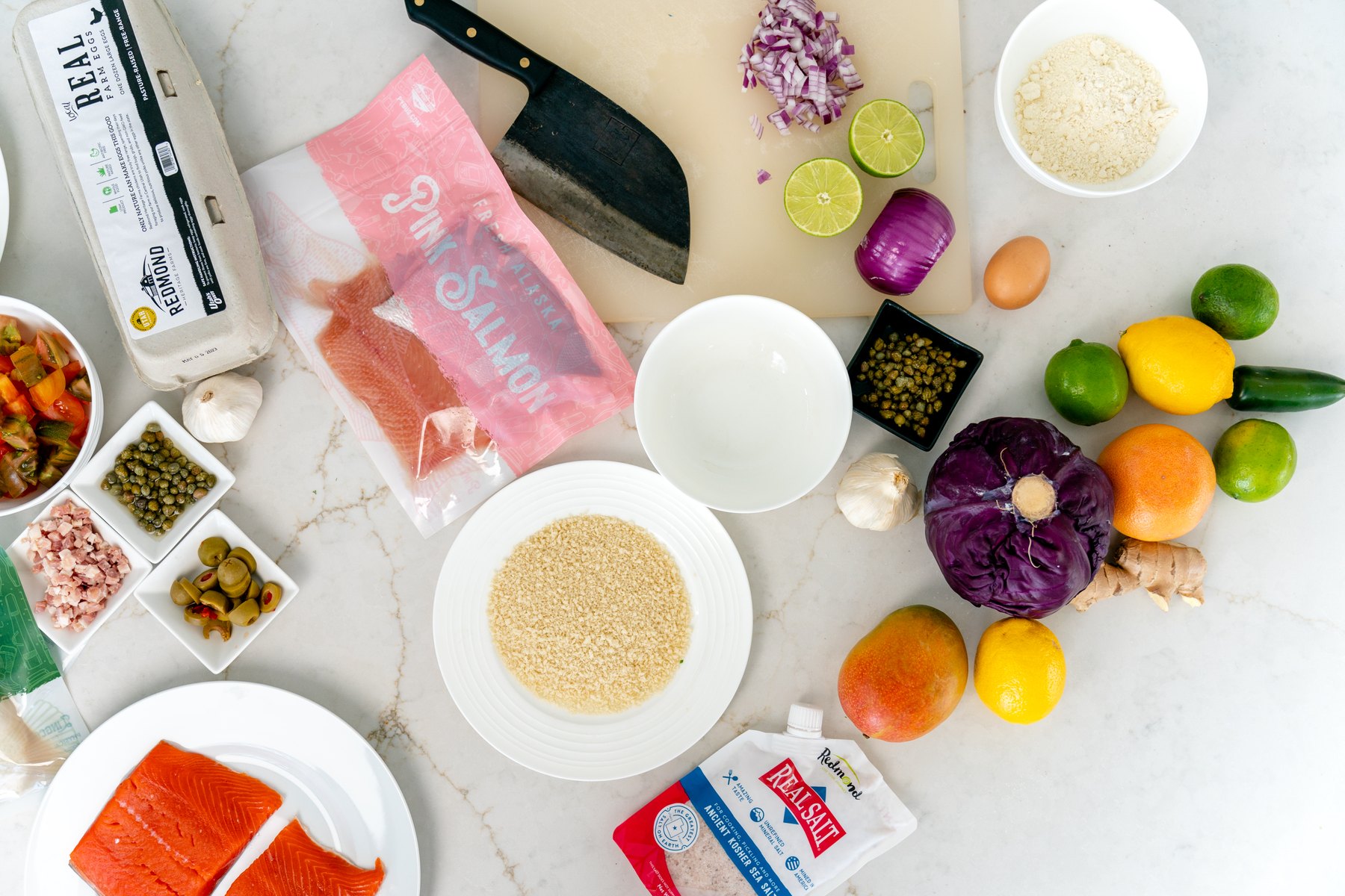 Salmon fillet, panko, capers, mango and the rest of the salmon cake ingredients laid out on a marble counter