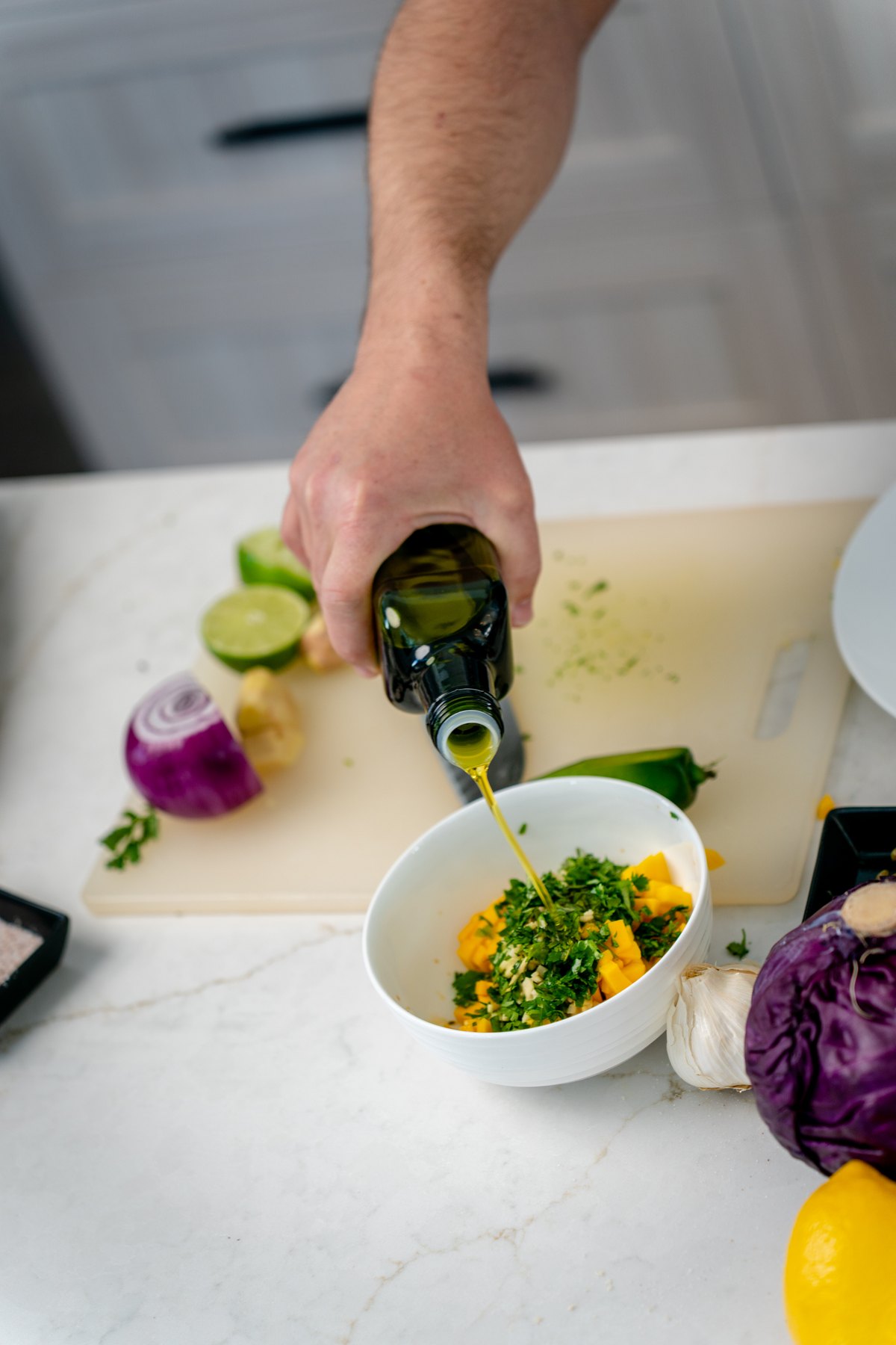 Pouring olive oil into a white bowl of diced mango, cilantro and red onion