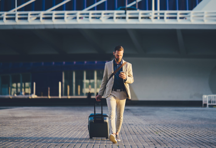A man with a suitcase walking while looking at his phone.
