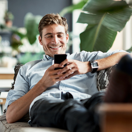 Man relaxing on his sofa smiling while booking stress-free parking in advance. 