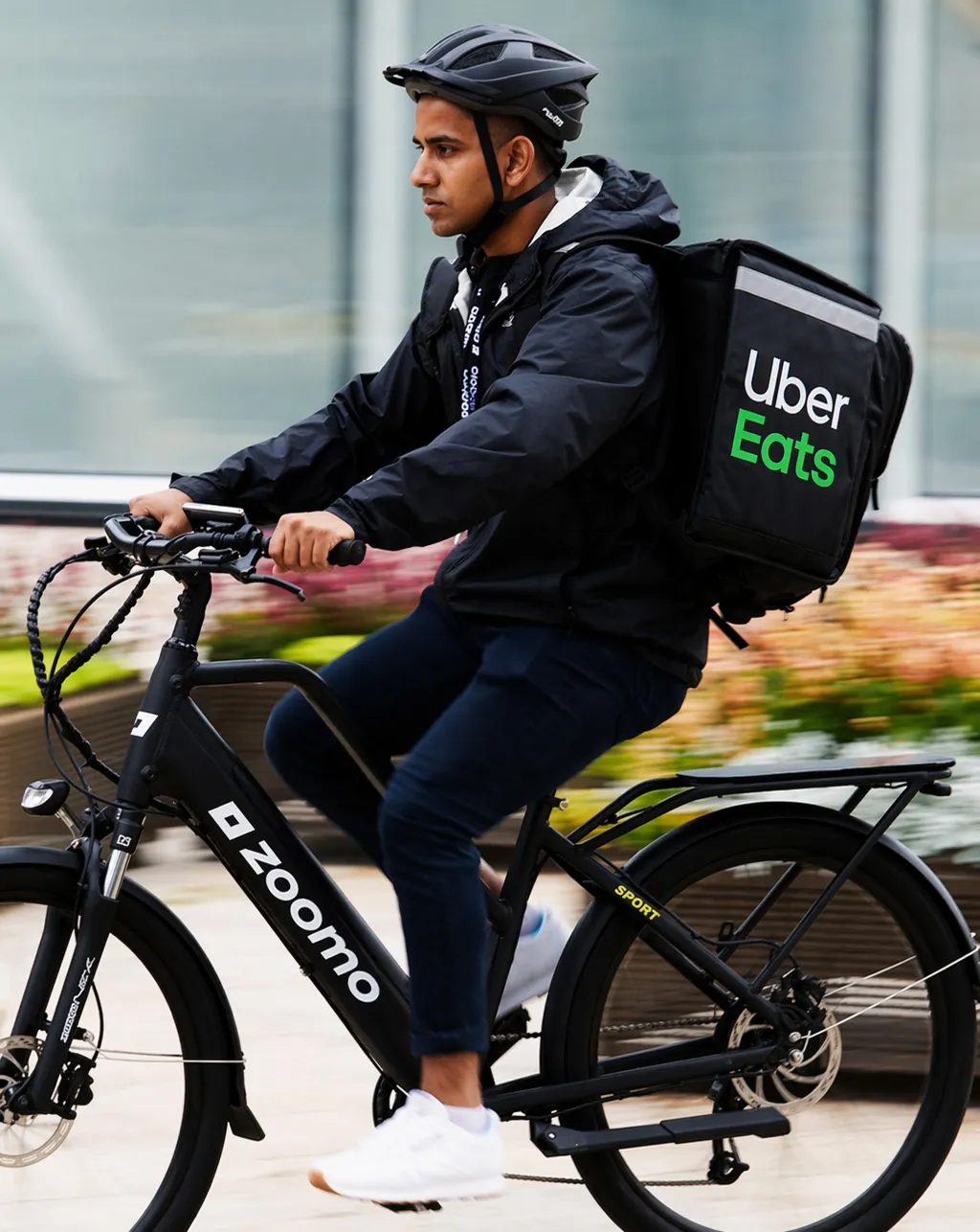 Two men in a workshop working on a white Zoomo electric bike with tools and parts scattered.