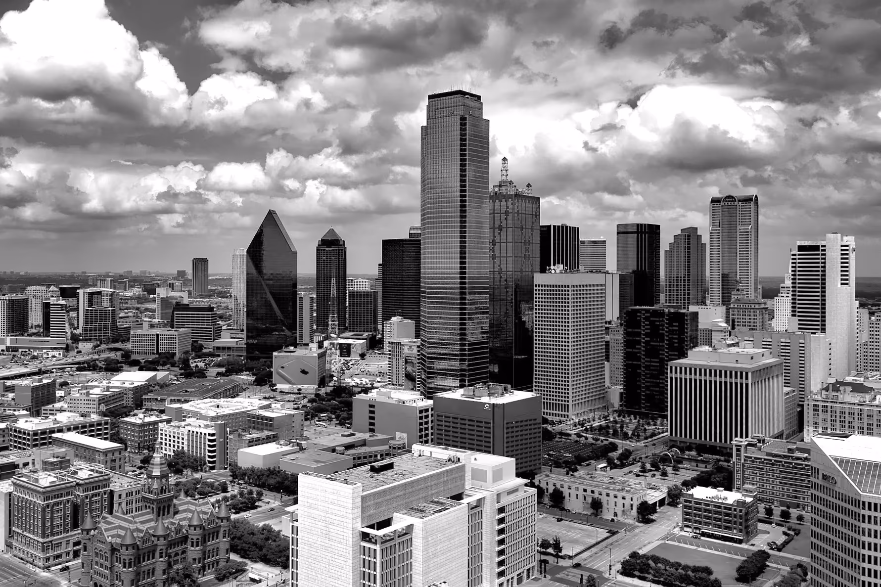 Black and white aerial view of a city skyline with tall skyscrapers and scattered clouds above.