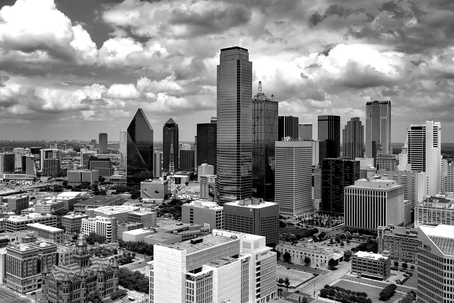 Black and white aerial view of a city skyline with tall skyscrapers and scattered clouds above.