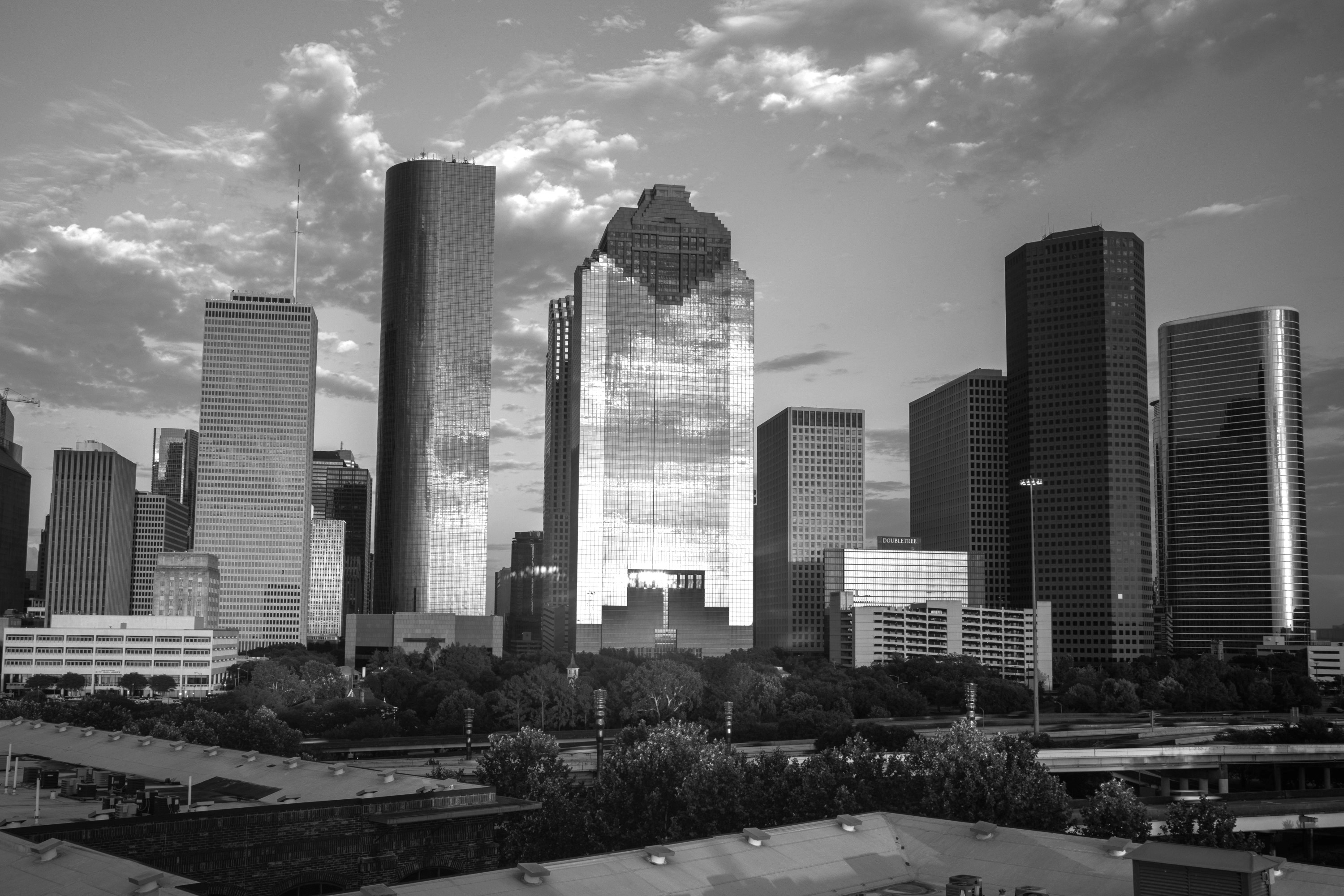 Black and white view of Houston skyline with tall reflected glass skyscrapers under a partly cloudy sky.