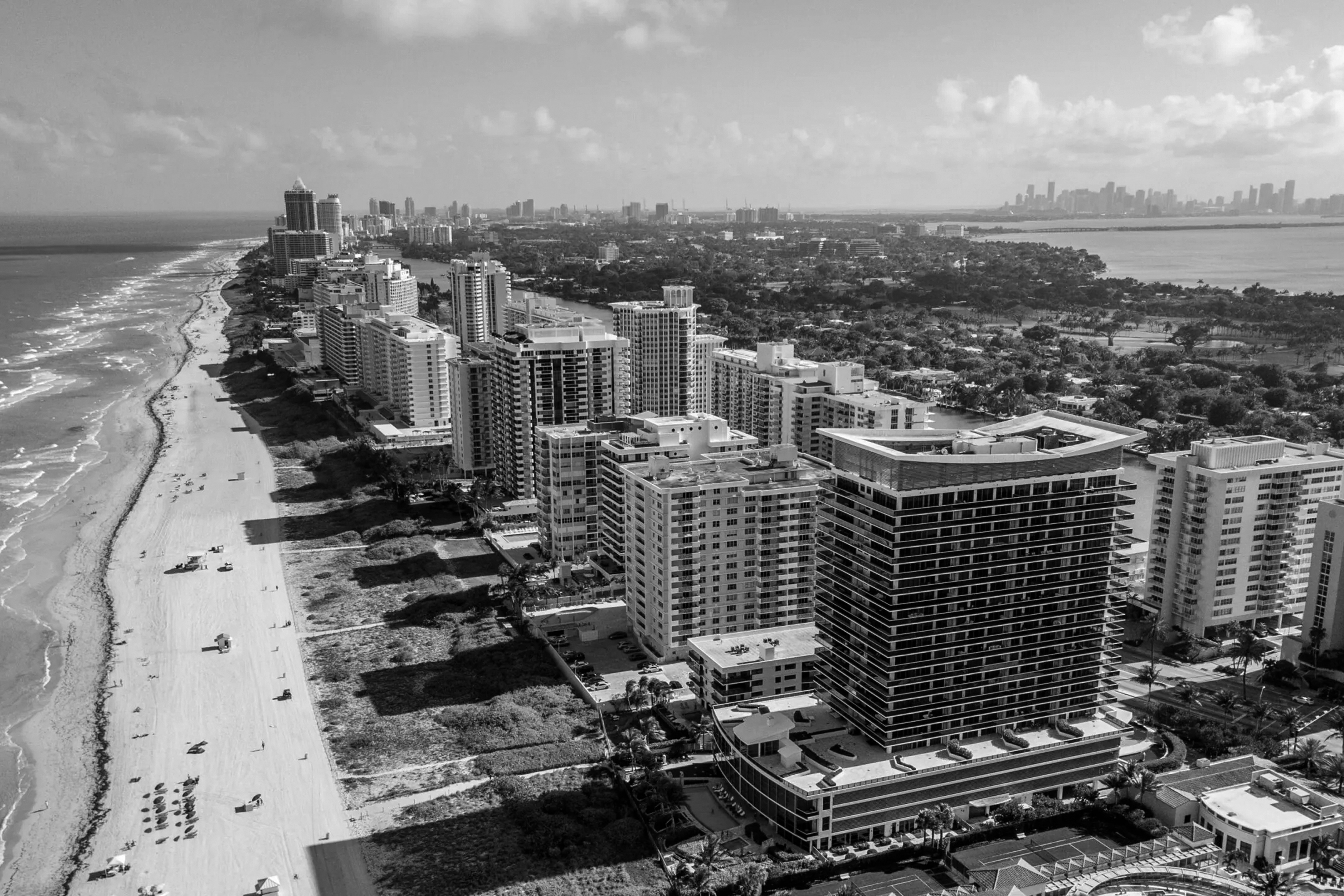 Aerial view of a coastal city with high-rise buildings along a sandy beach and the ocean on the left.
