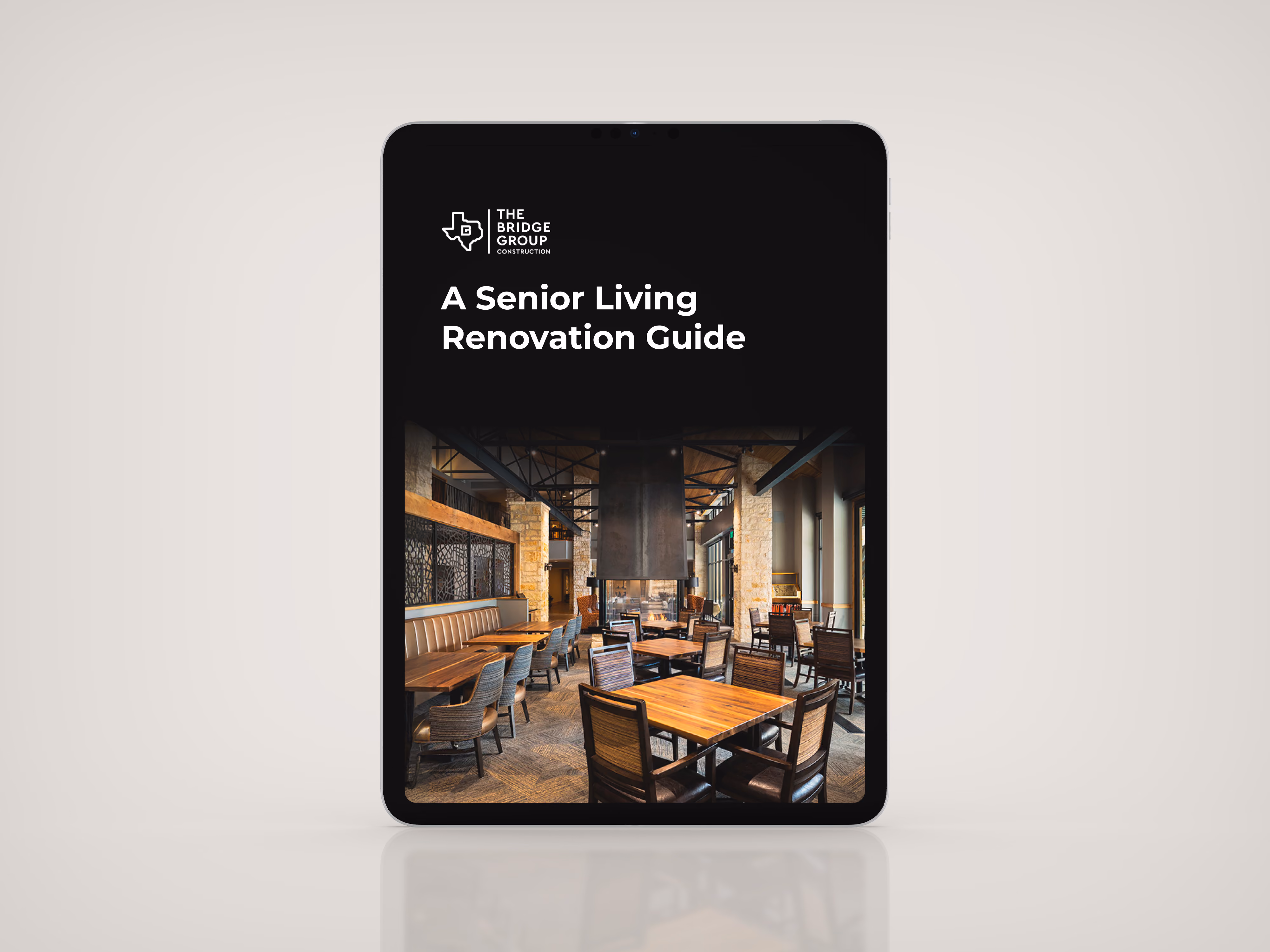 Tablet displaying cover of A Senior Living Renovation Guide by The Bridge Group Construction, featuring a modern dining area with wooden tables and chairs.