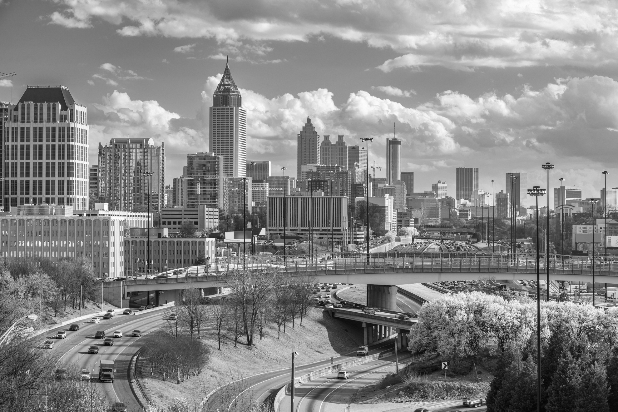 Black and white image of a city skyline with highways, bridges, and dense traffic under a partly cloudy sky.