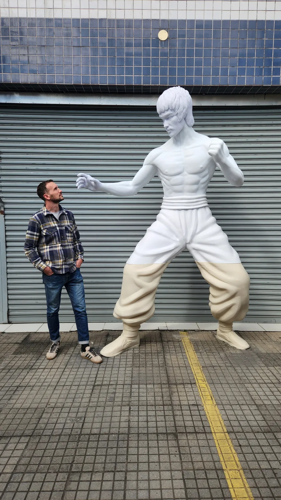 Escultura de gran formato de artista de artes marciales instalada en la calle, junto a una persona para escala, impresa en 3D en São Paulo