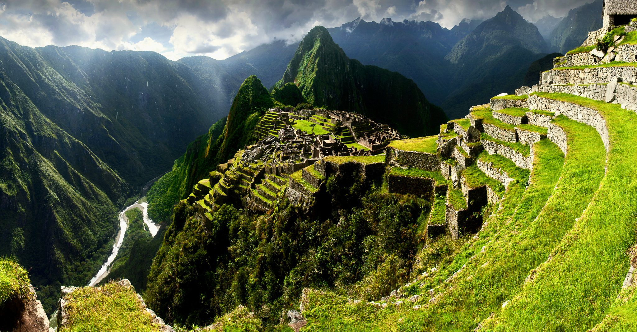 Panoramic view of the ancient Inca citadel Machu Picchu nestled high in the green Andes mountains with the Urubamba river valley below" caption="The ultimate reward: The mystical Inca estate of Machu Picchu basking in the mountain sunlight.