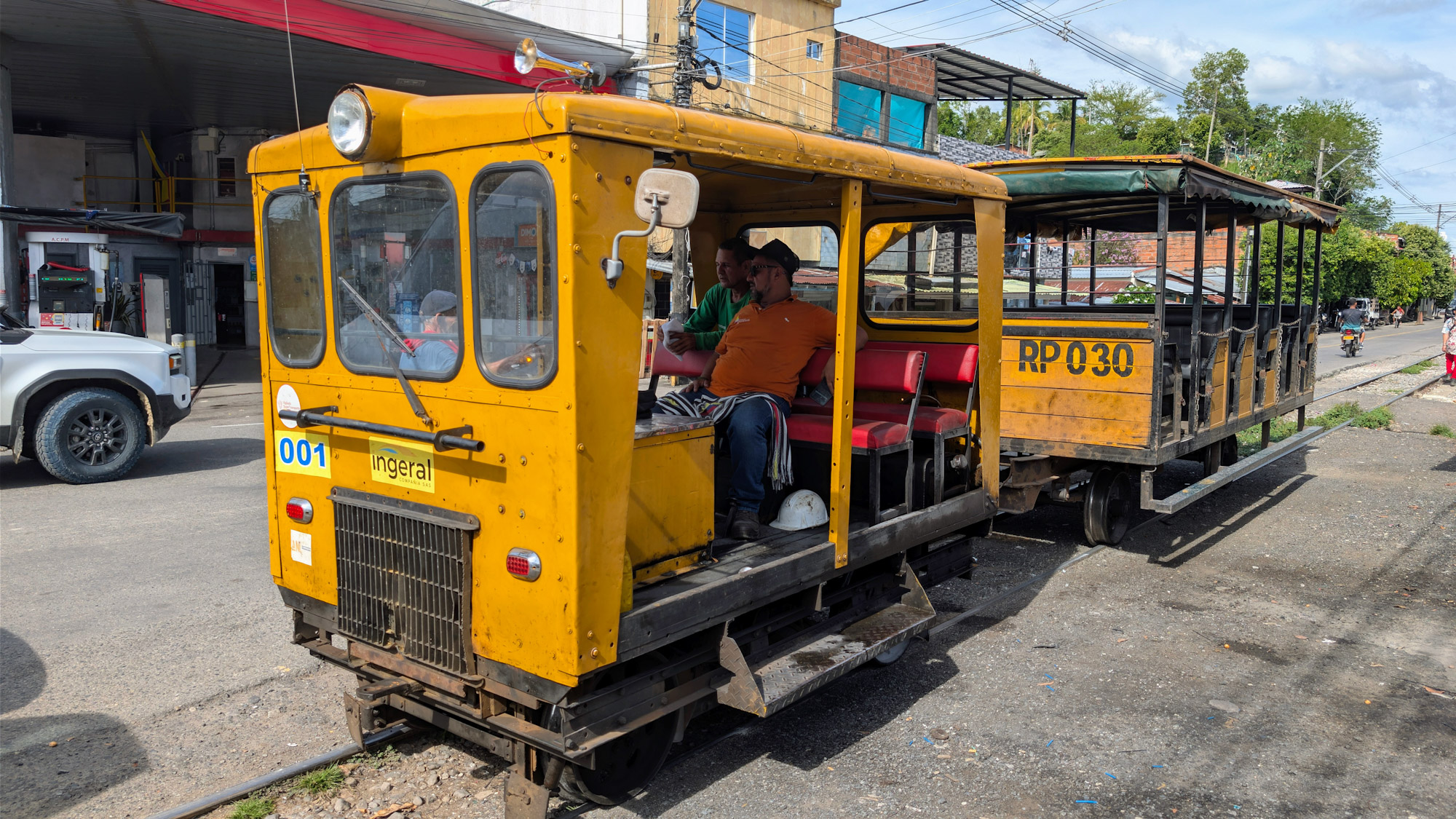 A yellow open-air carromotor rail vehicle with passenger carriage on the Magdalena Valley Railway line in Colombia.