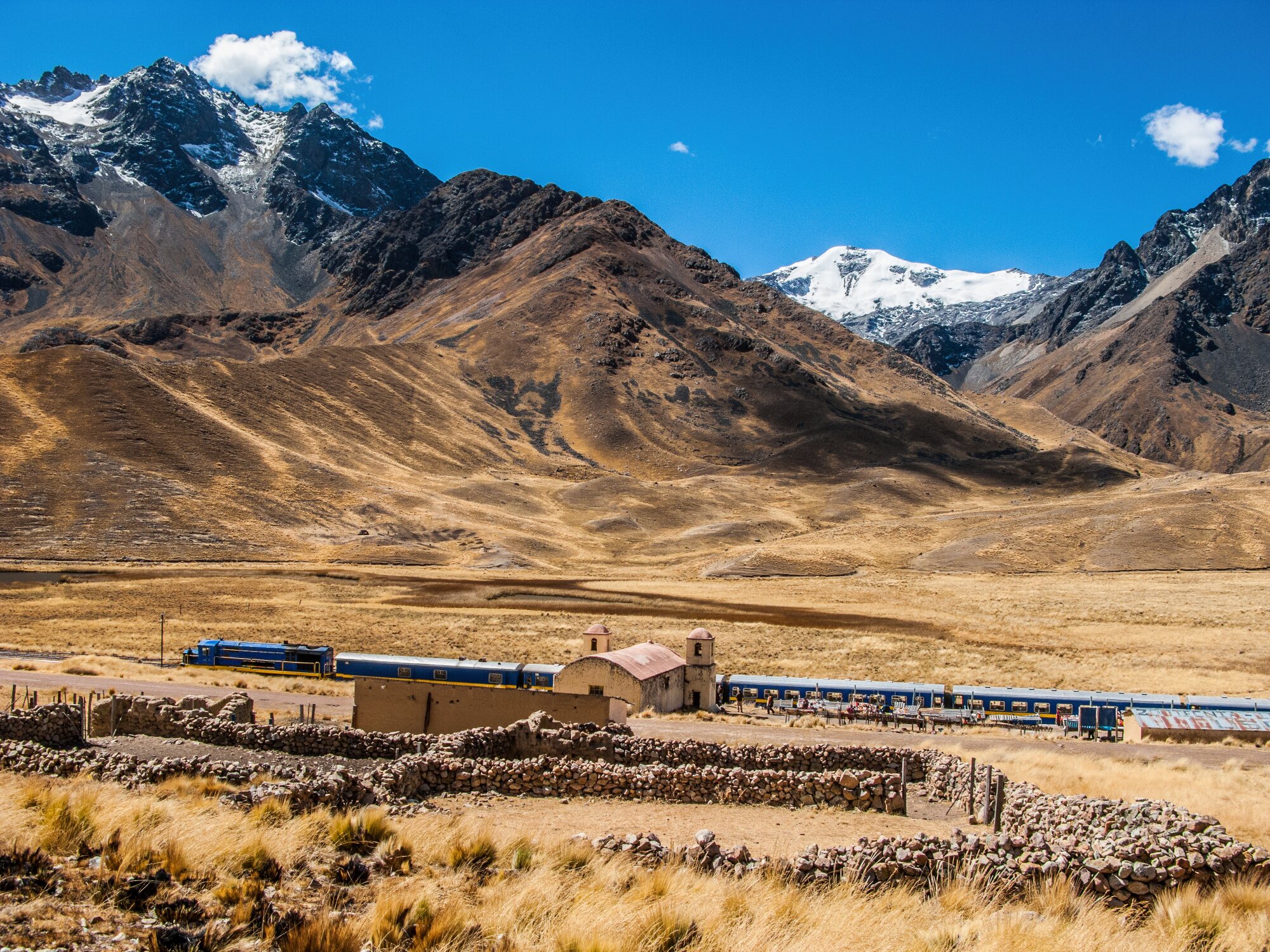 PeruRail Titicaca train at La Raya Pass beneath snow-capped mountains in the Peruvian Andes.