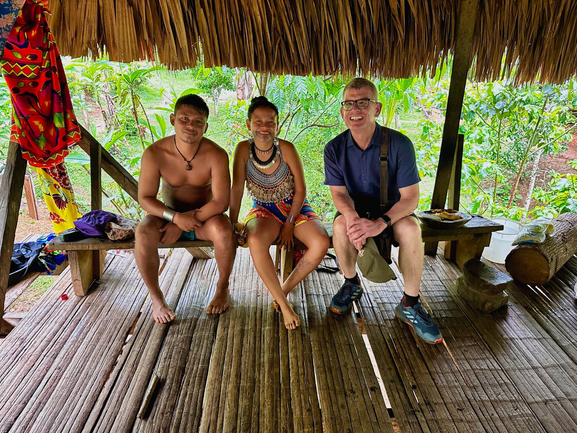 Rail South America tour leader seated with an Emberá couple under a traditional thatched shelter in Panama.