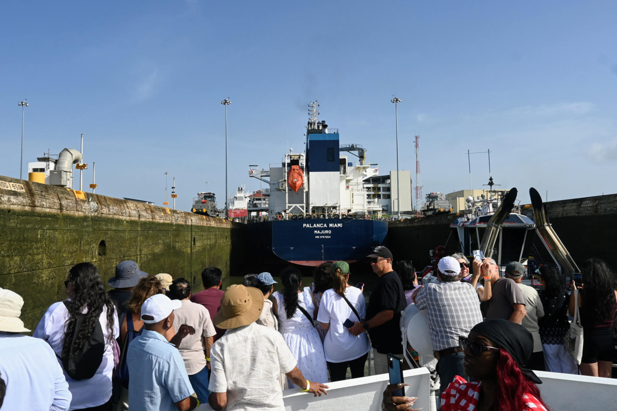 Passengers aboard a tour boat during a partial Panama Canal transit, approaching a large cargo ship inside the canal locks.